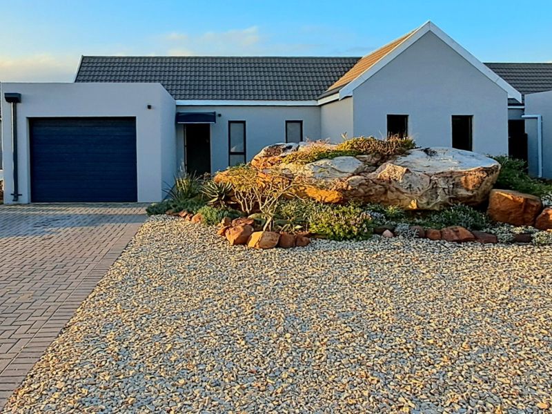 Modern single-story residential home featuring a paved driveway, integrated garage, and a well-maintained landscaped rock garden in the front yard.
