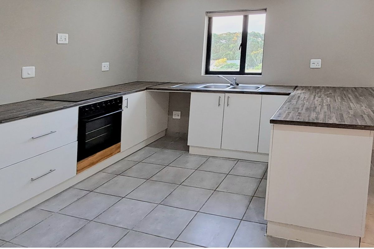 A clean, modern kitchen featuring white cabinetry, dark laminate countertops, a built-in oven, and tiled flooring with a functional layout.
