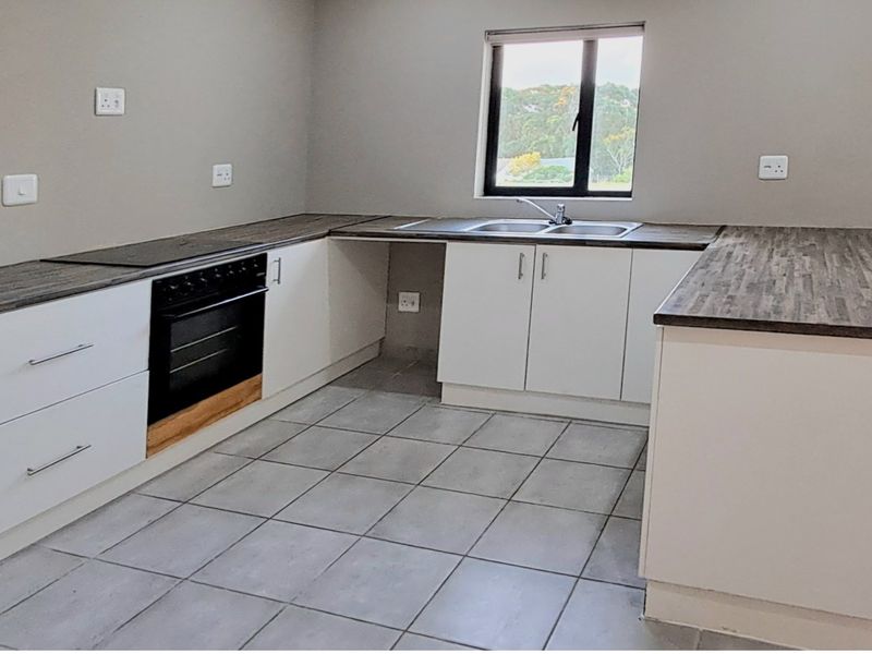 A clean, modern kitchen featuring white cabinetry, dark laminate countertops, a built-in oven, and tiled flooring with a functional layout.