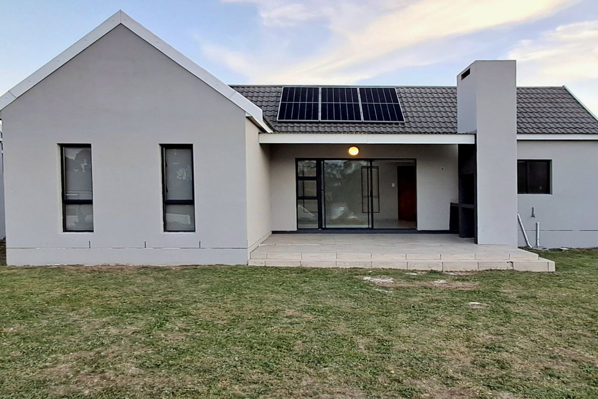 Rear view of a modern house featuring a covered patio with a built-in braai, sliding glass doors, and roof-mounted solar panels.