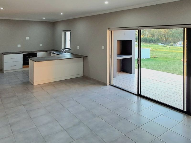 Spacious open-plan kitchen and living area featuring neutral tiled floors, modern cabinetry, and large sliding doors opening onto a patio with a built-in braai.