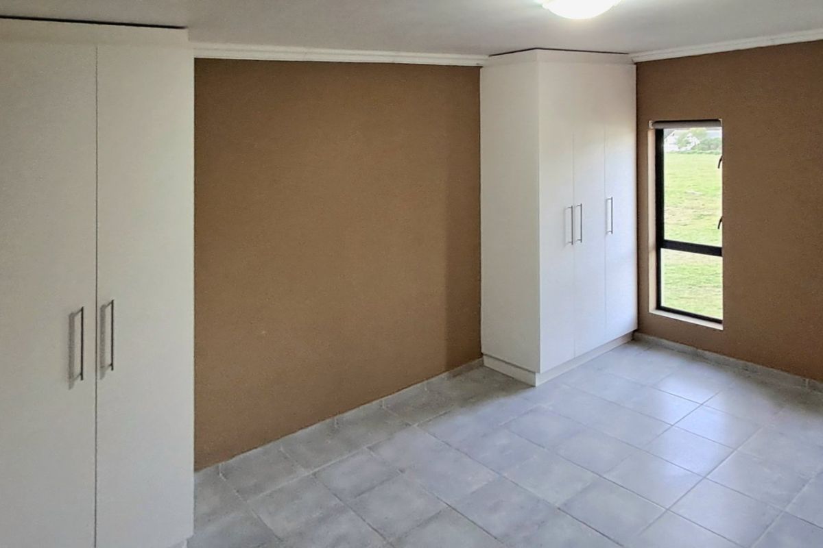 A vacant bedroom featuring neutral-toned walls, tiled flooring, and ample built-in cupboard storage with views of the surrounding garden.