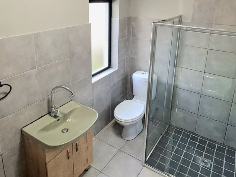 A functional bathroom featuring a glass shower enclosure, wall-mounted basin, and toilet with neutral wall and floor tiling.
