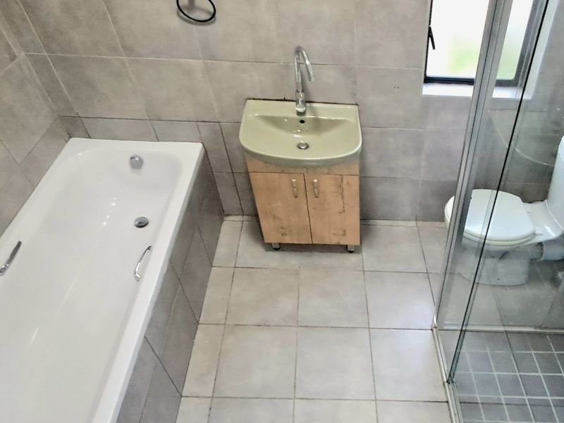 A functional bathroom featuring a bathtub, separate shower enclosure, toilet, and a vanity unit with a washbasin, finished with neutral wall and floor tiles.