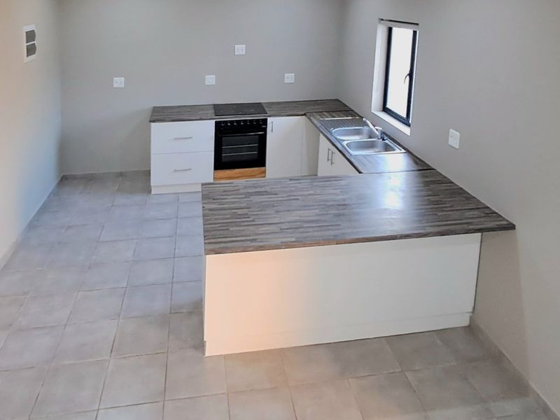 A clean, modern kitchen featuring white cabinetry, dark laminate countertops, a built-in oven and hob, and neutral tiled flooring.
