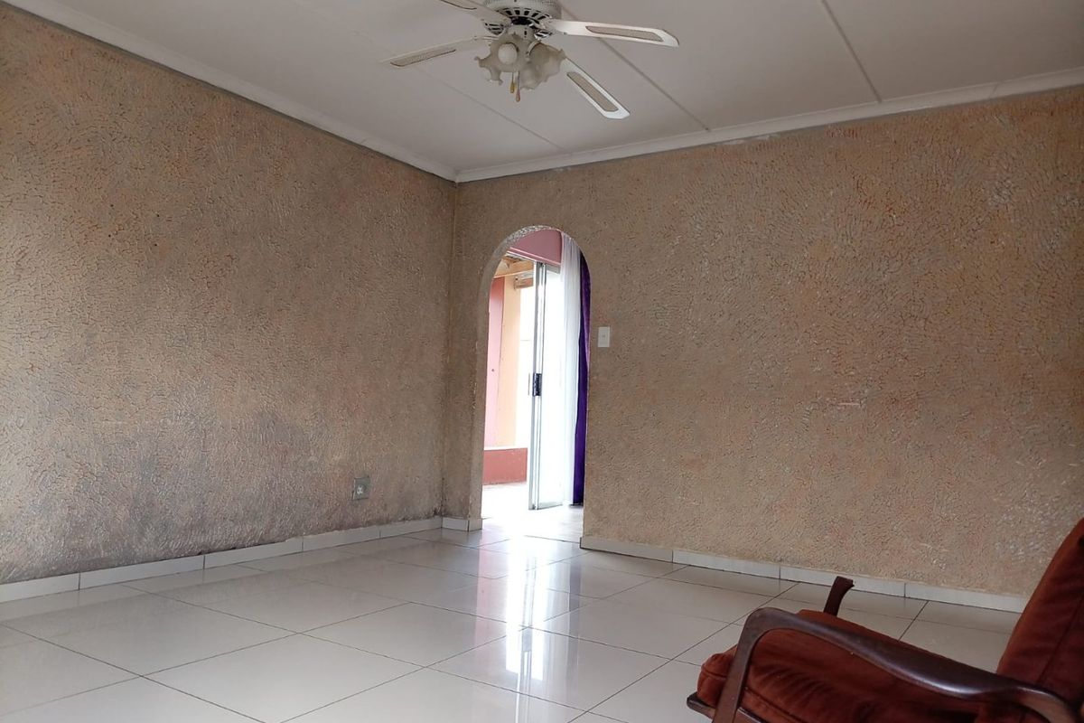 An empty living room featuring tiled flooring, a ceiling fan, and a distinctive arched doorway leading to an adjacent space.