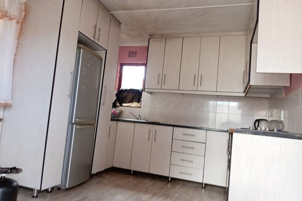 A functional kitchen featuring light-toned laminate cabinetry, tiled backsplash, and a stainless steel sink, requiring some cosmetic updates to the ceiling and finishes.