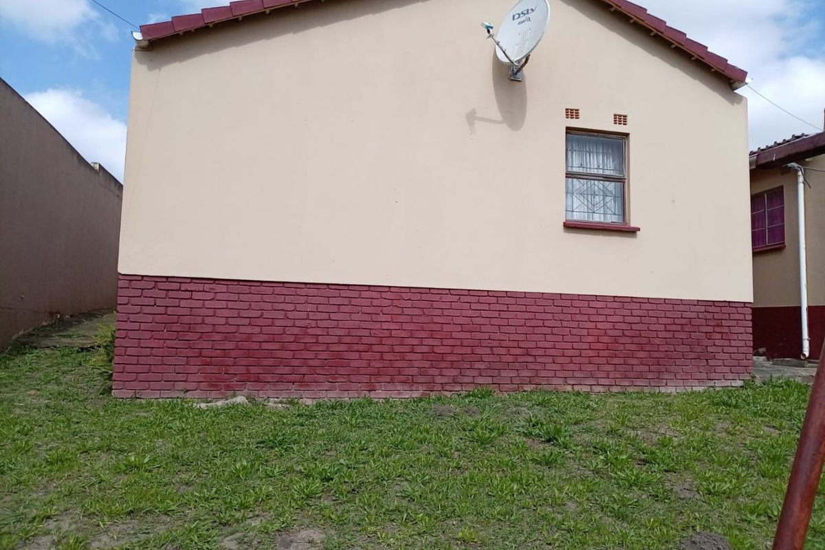 A view of the rear exterior wall featuring a brick plinth, plastered finish, a single window with burglar bars, and a mounted satellite dish.