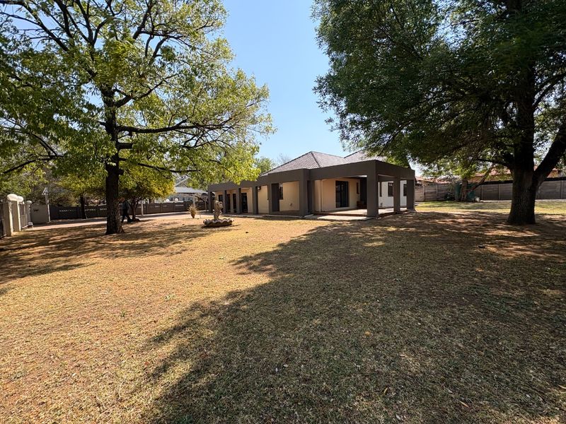 Spacious rear garden featuring a large lawn, mature trees, and a covered patio area attached to the main house structure.
