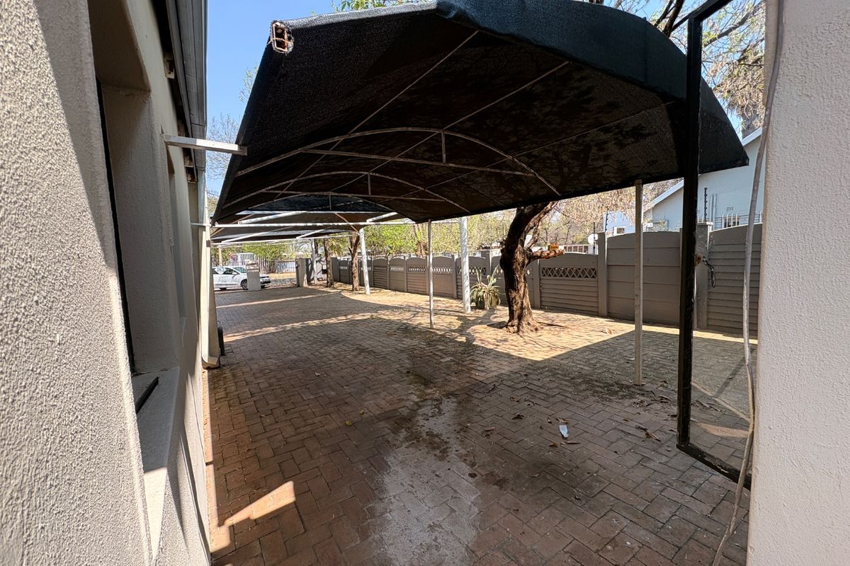 A paved outdoor area featuring a large shade cloth carport structure and enclosed by precast concrete boundary walls.