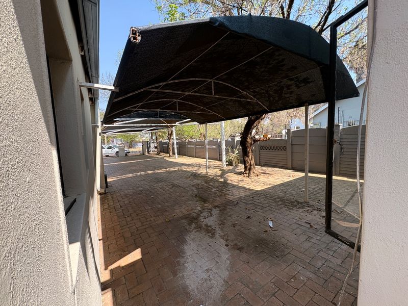 A paved outdoor area featuring a large shade cloth carport structure and enclosed by precast concrete boundary walls.