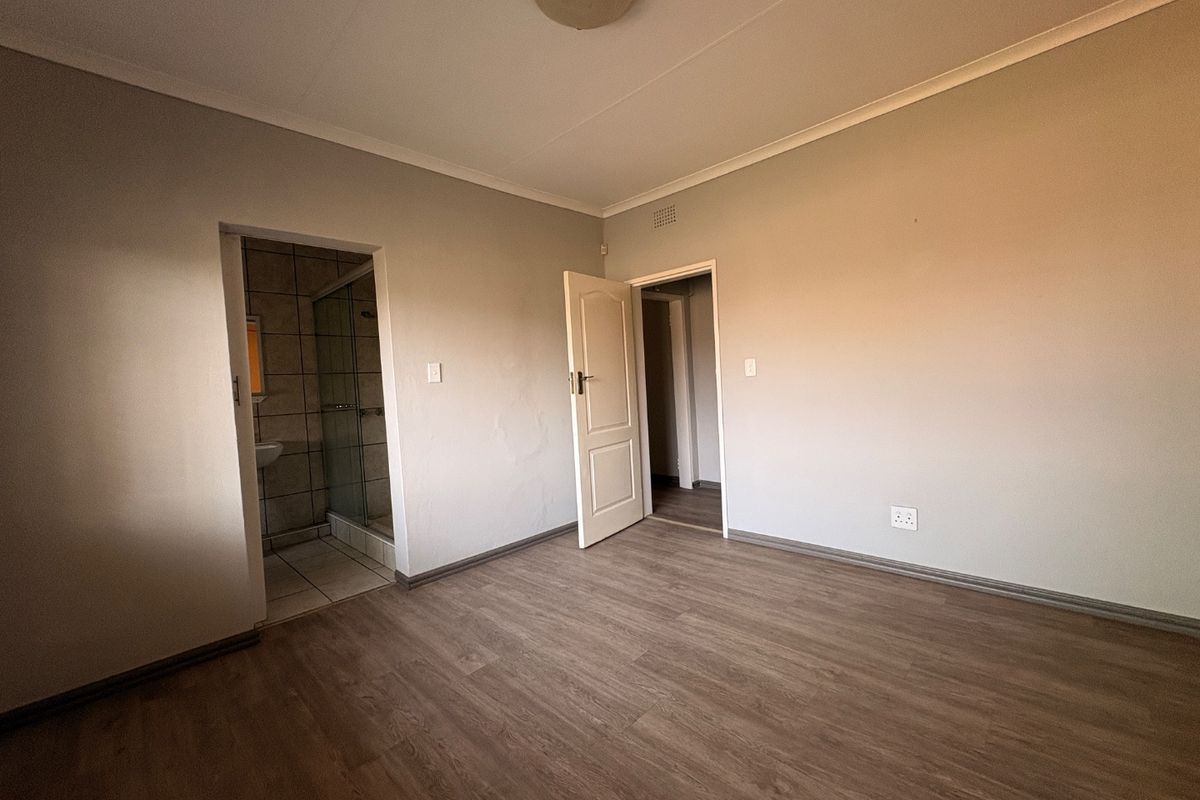 An empty bedroom featuring laminate flooring, a neutral color palette, and an adjoining en-suite bathroom with a shower.