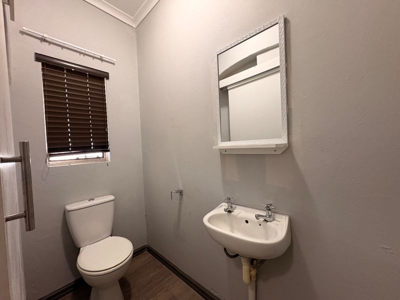 A functional guest bathroom featuring a wall-mounted basin, toilet, and mirror, finished with neutral wall tones and wood-look flooring.