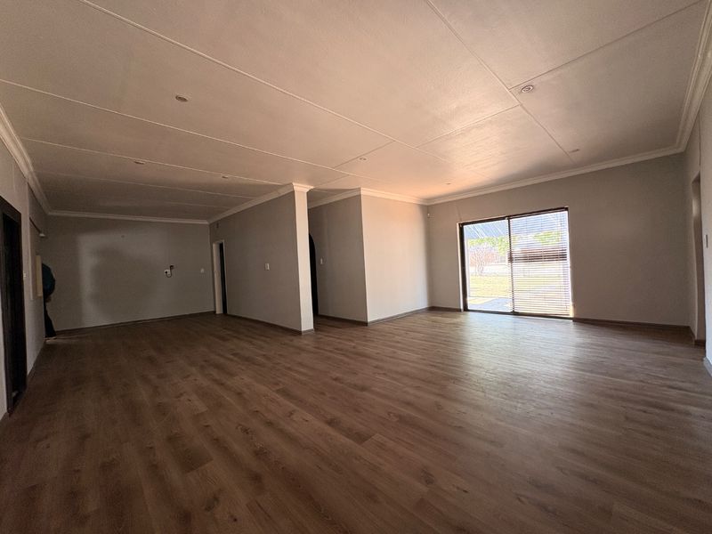 Spacious, open-plan living area featuring modern laminate flooring, recessed ceiling lighting, and a large sliding glass door providing natural light and garden access.