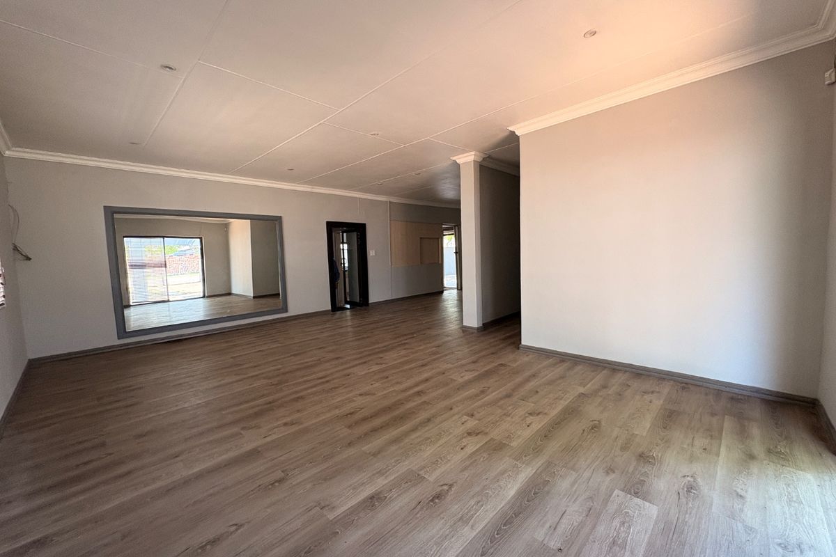 A spacious, empty living area featuring modern laminate flooring, recessed lighting, and a large wall-mounted mirror, offering a clean and versatile blank canvas.