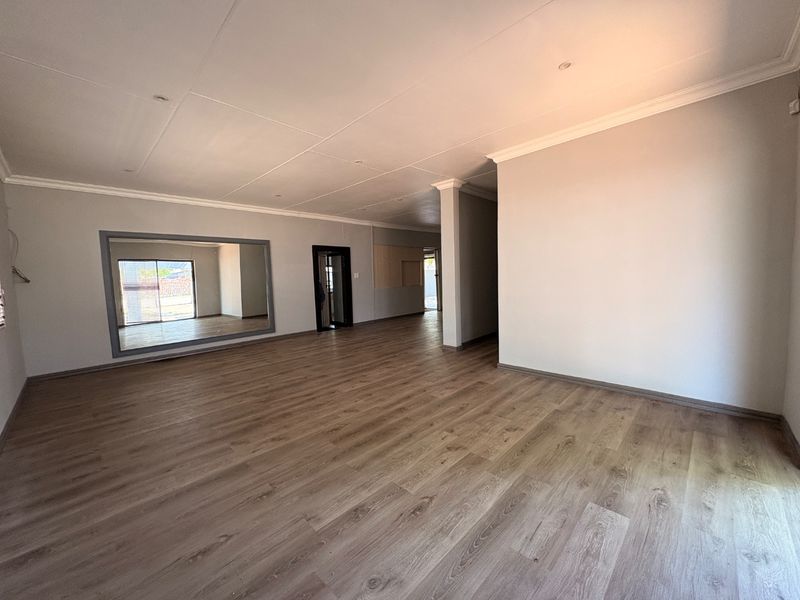 A spacious, empty living area featuring modern laminate flooring, recessed lighting, and a large wall-mounted mirror, offering a clean and versatile blank canvas.