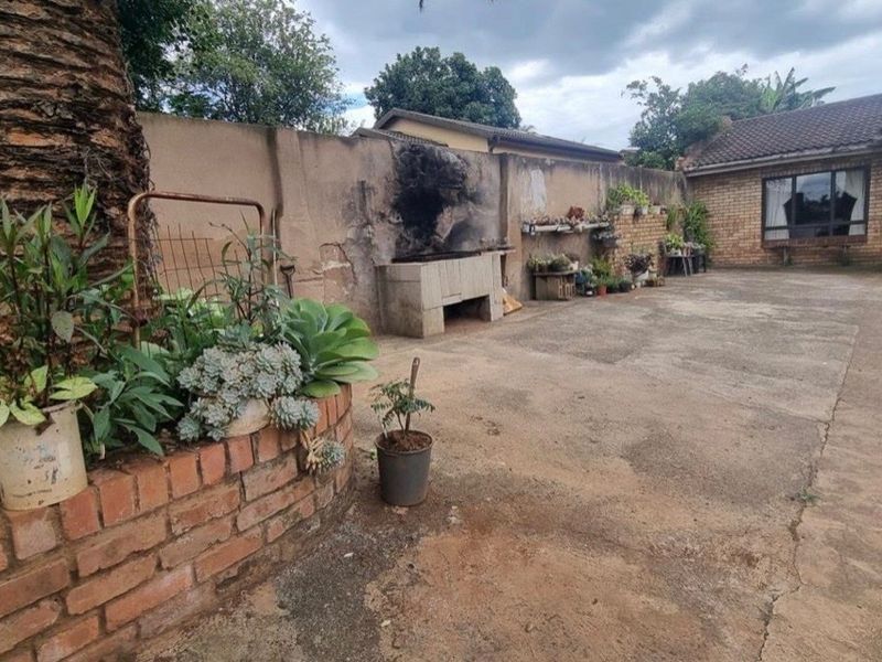Rear exterior area featuring a paved courtyard, brick boundary wall, and a built-in braai facility.