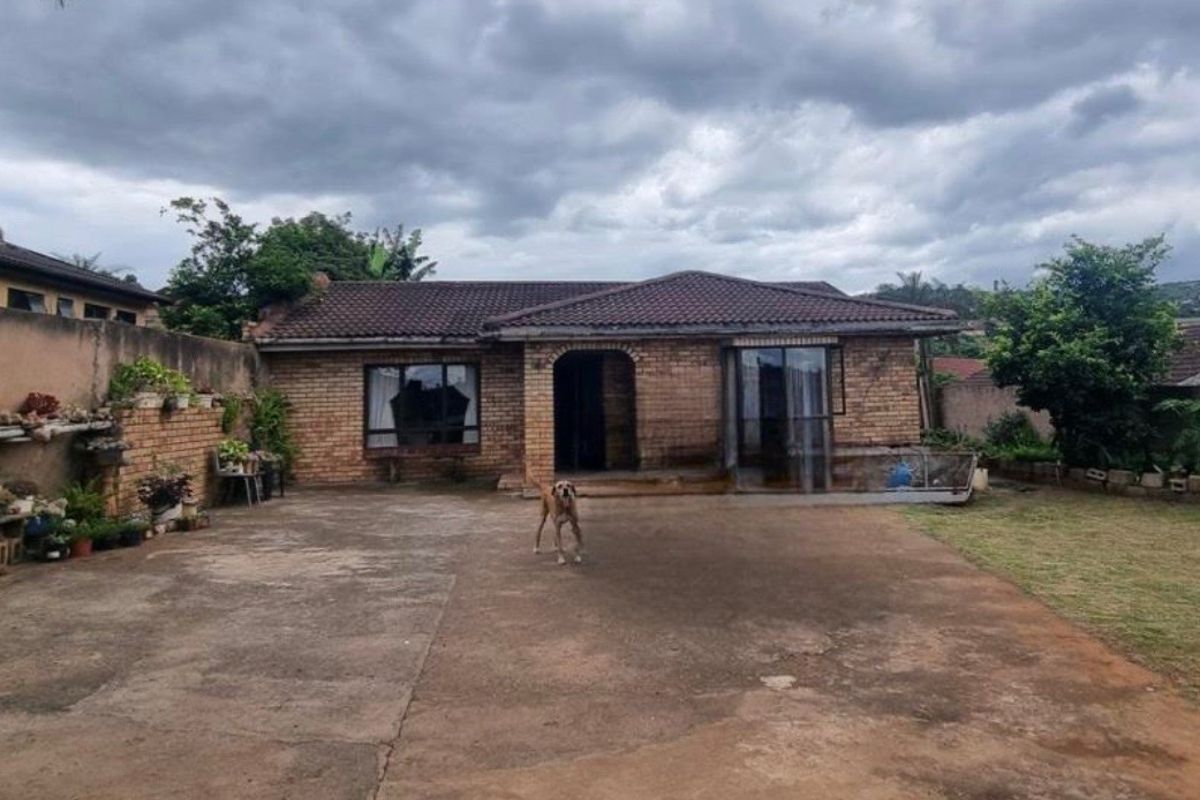 Rear view of a single-story brick house featuring a tiled roof, concrete driveway, and a sliding glass door entrance.