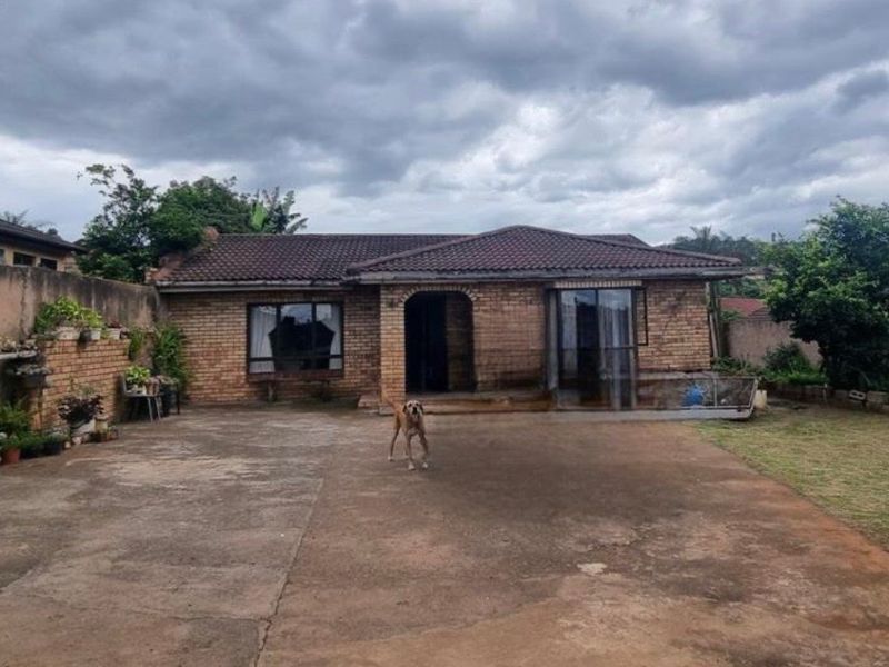 Rear view of a single-story brick house featuring a tiled roof, concrete driveway, and a sliding glass door entrance.