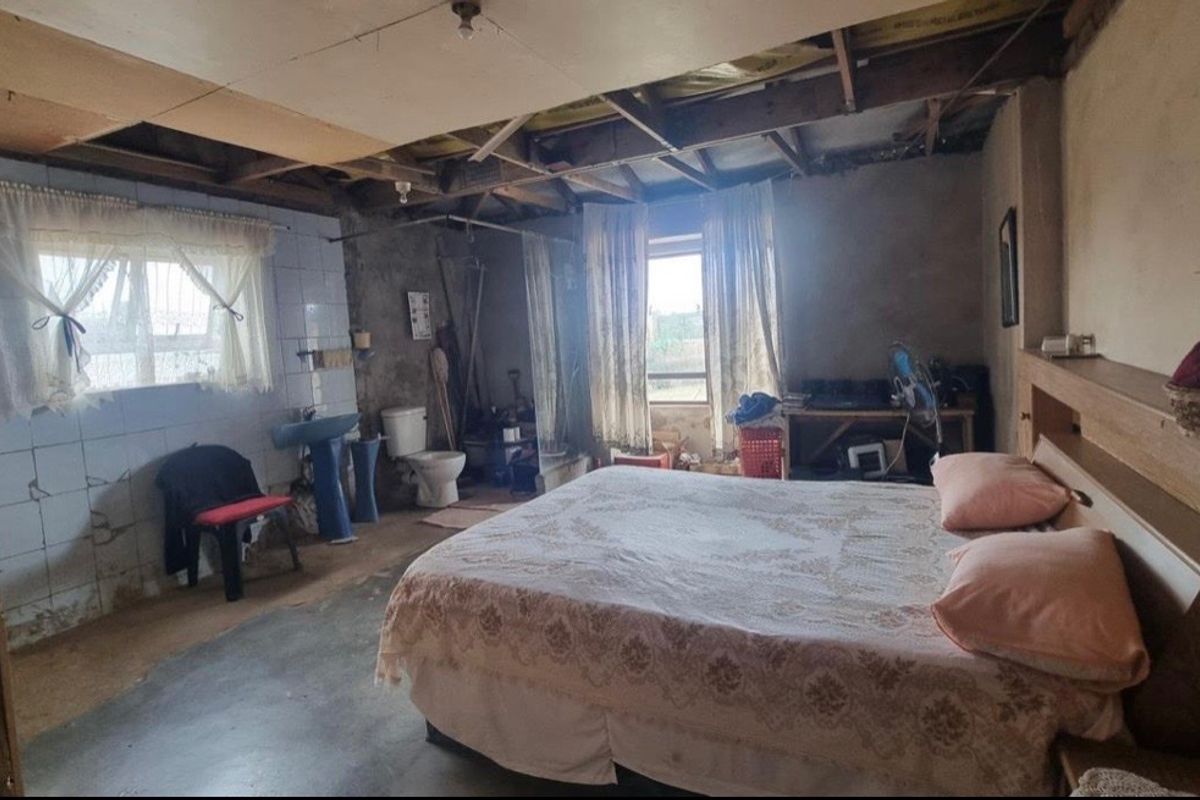 A bedroom featuring exposed ceiling rafters and unfinished wall surfaces, including an integrated basin and toilet area requiring significant renovation and repair.