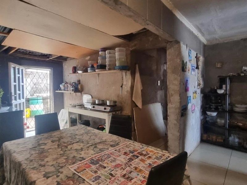 Open plan living and dining area featuring tiled floors, security gate access, and unfinished wall and ceiling surfaces requiring renovation.