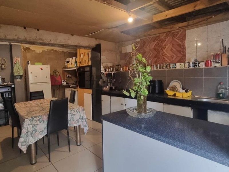 Open-plan kitchen and dining area featuring built-in cabinetry and island, currently requiring significant renovation to address unfinished ceilings and wall surfaces.