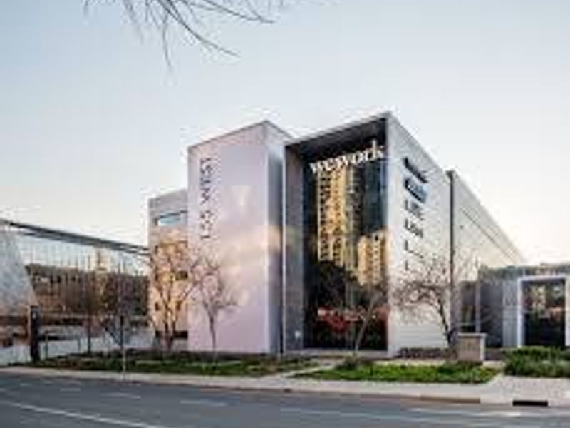 Modern commercial office building facade featuring large glass windows, prominent signage, and well-maintained street-level landscaping.