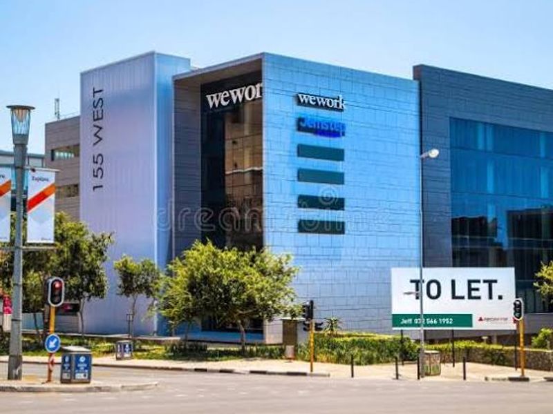 Front exterior view of a modern commercial office building featuring glass facades, metal cladding, and prominent signage.