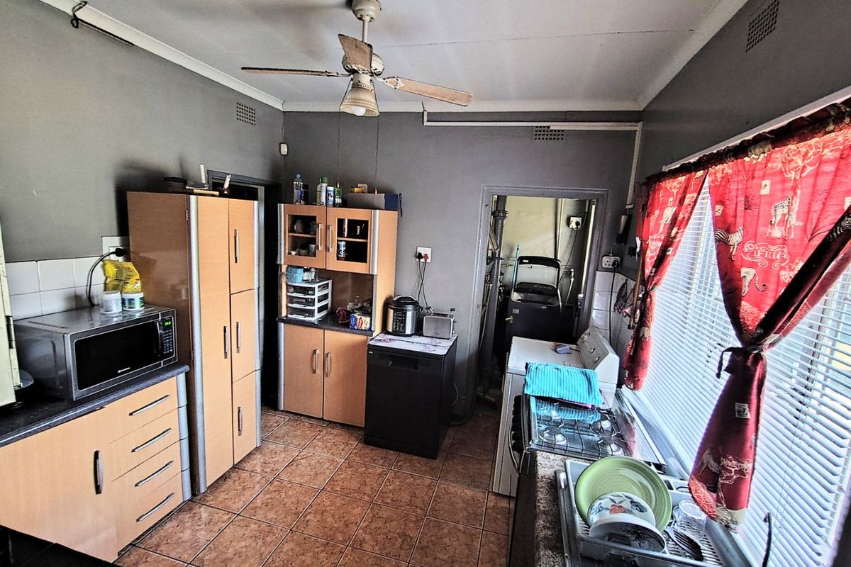 A functional kitchen featuring built-in cabinetry, a gas hob, tiled flooring, and a ceiling fan, with an adjacent utility area visible.