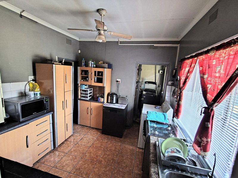A functional kitchen featuring built-in cabinetry, a gas hob, tiled flooring, and a ceiling fan, with an adjacent utility area visible.