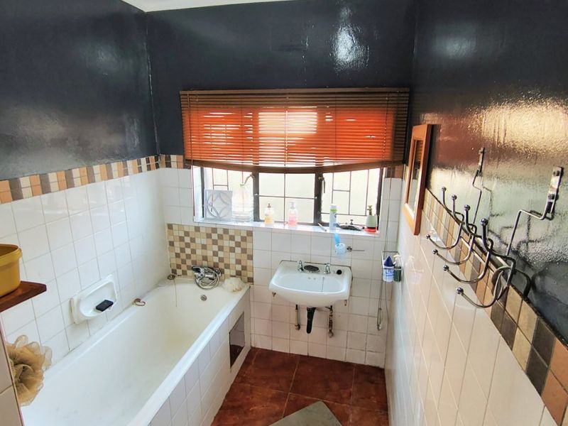 A compact bathroom featuring a bathtub, wall-mounted basin, and tiled finishes, offering potential for a modern renovation to enhance the space.