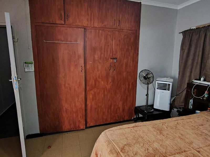 A bedroom featuring built-in wooden cupboards, a ceiling fan, and tiled flooring, offering a functional space with potential for cosmetic updates.
