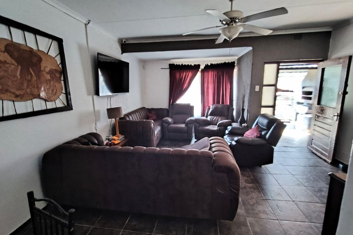Spacious living room featuring tiled flooring, a ceiling fan, and an exposed beam, with direct access to an outdoor patio area.