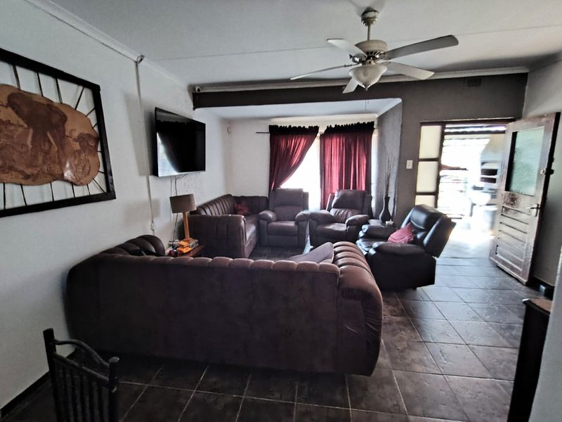 Spacious living room featuring tiled flooring, a ceiling fan, and an exposed beam, with direct access to an outdoor patio area.