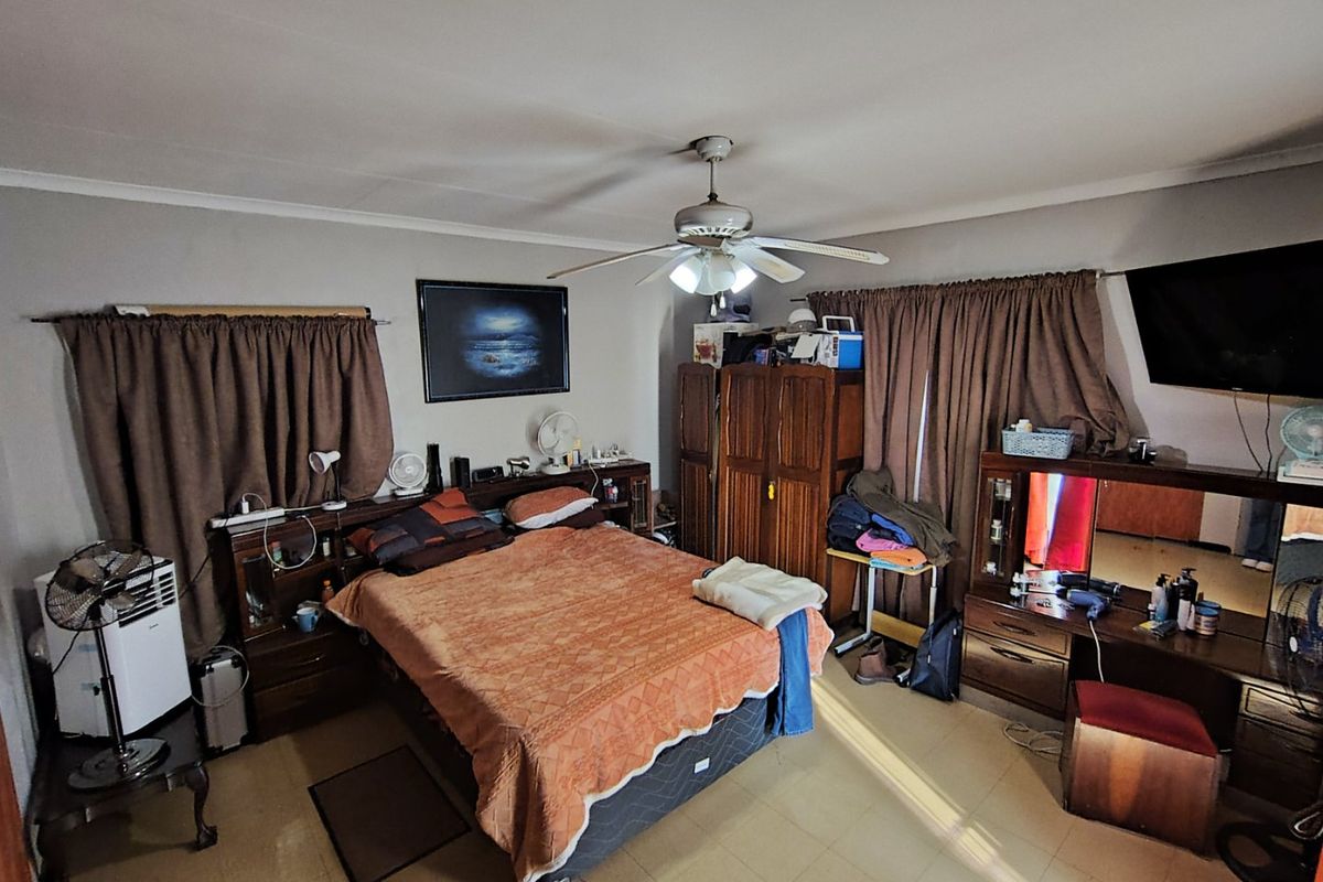 A spacious bedroom featuring tiled flooring and a central ceiling fan, offering a functional layout with ample space for bedroom furniture.