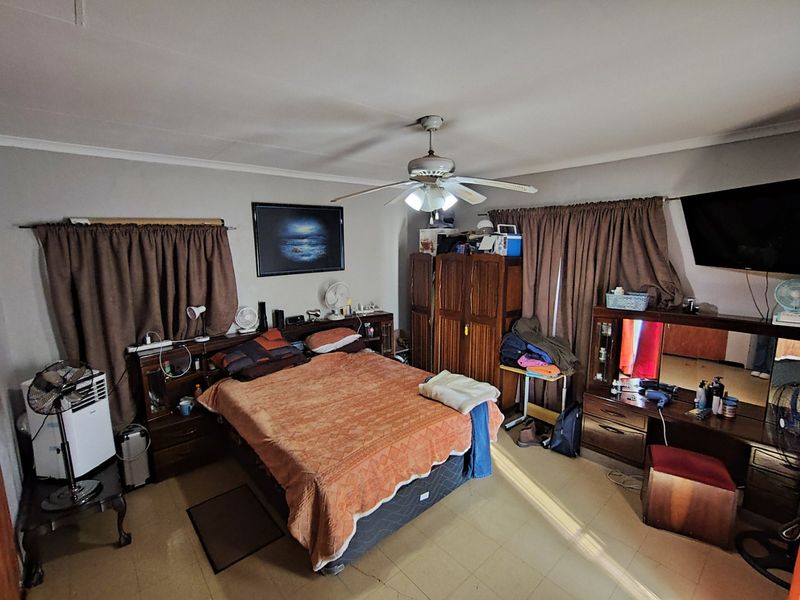 A spacious bedroom featuring tiled flooring and a central ceiling fan, offering a functional layout with ample space for bedroom furniture.
