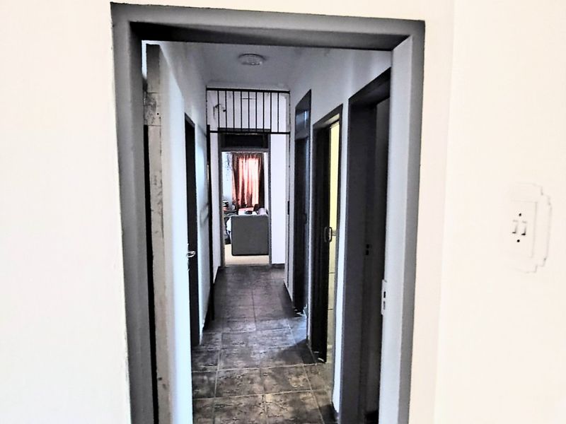A narrow interior hallway featuring tiled flooring and multiple doorways leading to other rooms, with a security gate installed at the end.