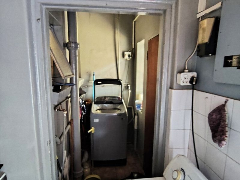 A functional laundry area featuring exposed plumbing, tiled splashbacks, and an electrical distribution board, requiring cosmetic updates to improve the space.