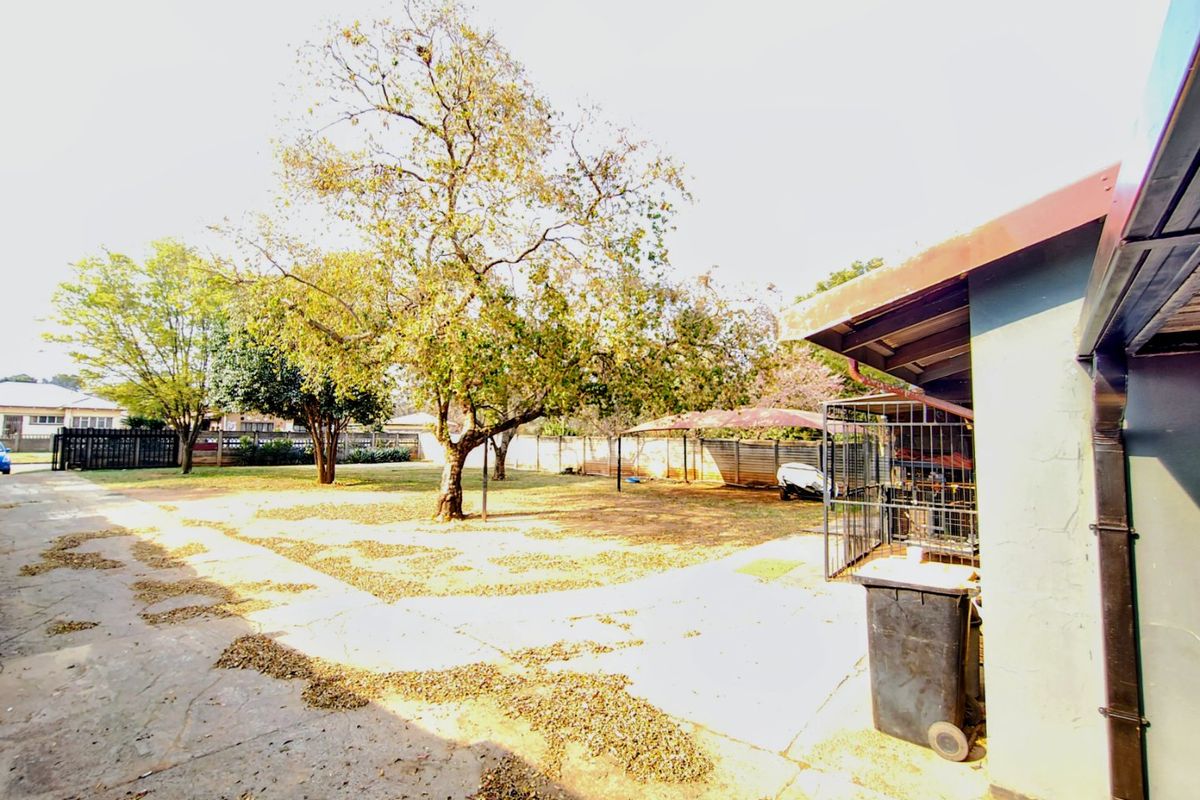 Spacious rear yard featuring concrete paving, mature trees, and a metal carport structure, offering potential for landscaping and outdoor improvement.