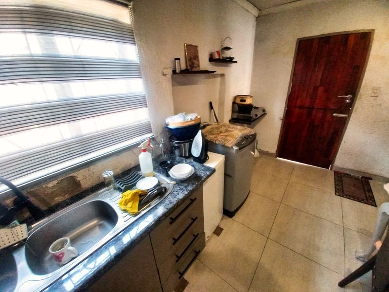 A functional laundry area featuring a stainless steel sink, laminate countertop, base cabinetry, and tiled flooring, with direct access to an exterior door.