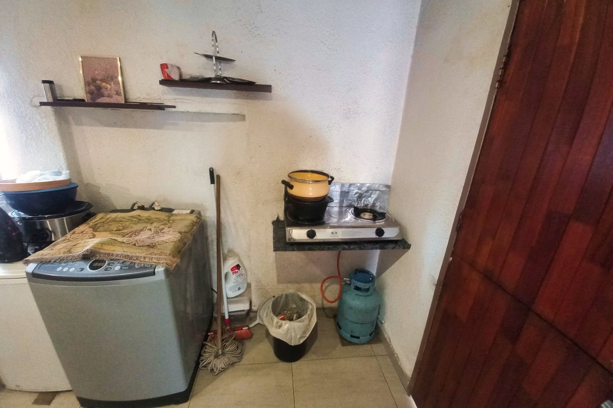 A compact kitchen area featuring a gas hob, tiled flooring, and a timber door, requiring cosmetic updates to improve the overall finish.