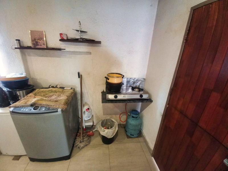 A compact kitchen area featuring a gas hob, tiled flooring, and a timber door, requiring cosmetic updates to improve the overall finish.