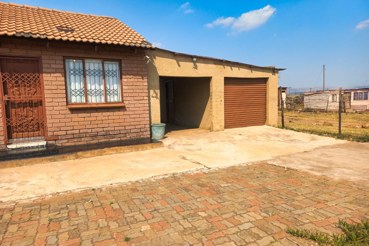Front exterior view of a brick house featuring a tiled roof, security gate, and an attached garage with a paved driveway.
