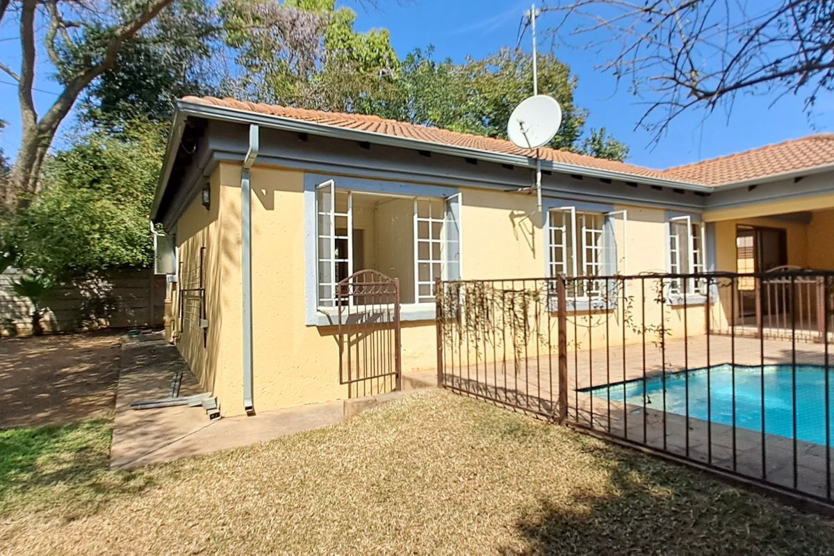 Rear exterior view of the house featuring a swimming pool with safety fencing, a paved patio area, and established garden surroundings.