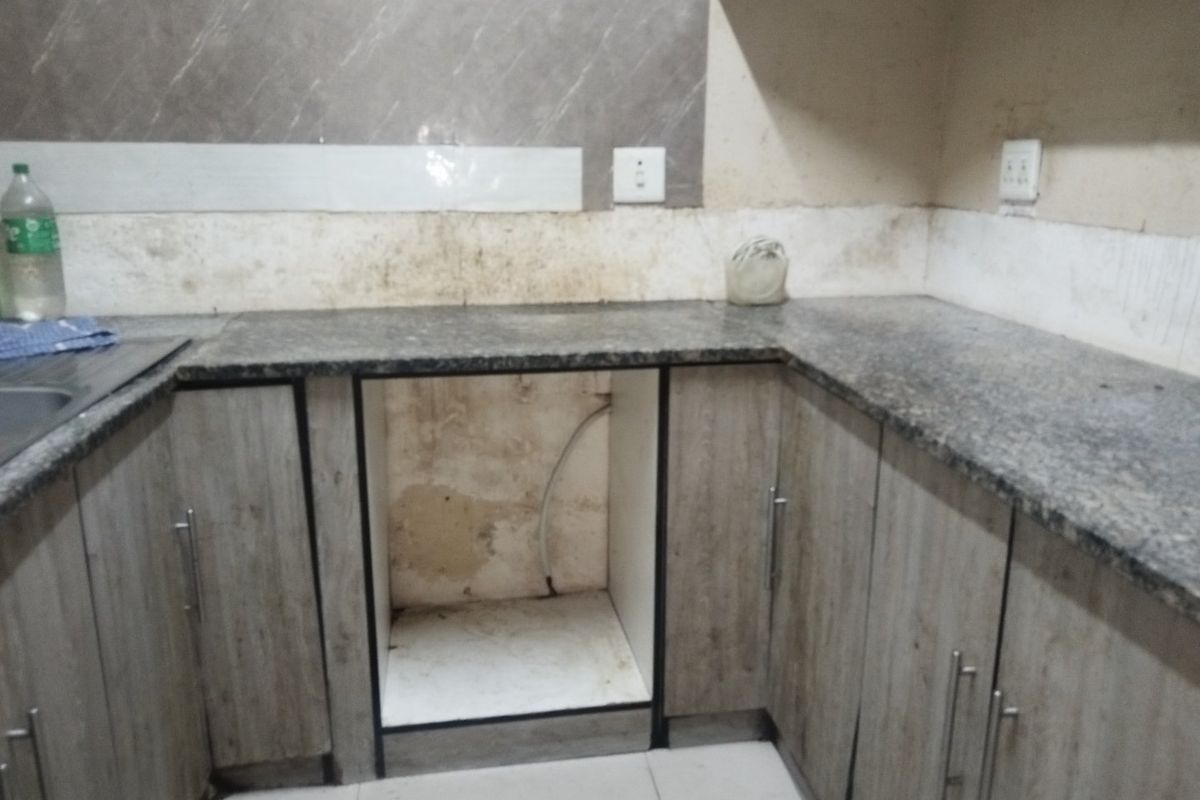 A compact kitchen area featuring granite countertops, wood-look cabinetry, and a tiled backsplash, currently requiring wall repairs and maintenance.