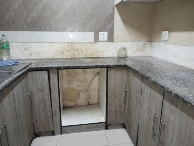 A compact kitchen area featuring granite countertops, wood-look cabinetry, and a tiled backsplash, currently requiring wall repairs and maintenance.