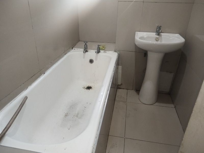 A functional bathroom featuring a standard bathtub and a pedestal basin with tiled walls and flooring, currently requiring maintenance and cosmetic updates.