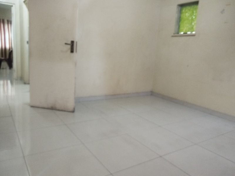 An empty bedroom featuring tiled flooring, a standard internal door, and a small window, requiring cosmetic updates to improve its overall condition.
