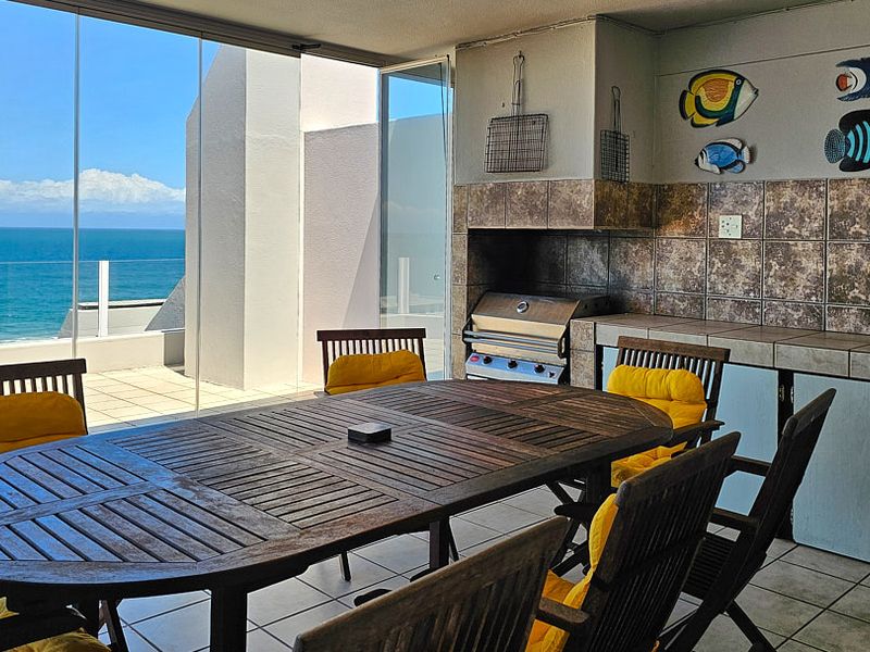 Covered balcony featuring a built-in braai, tiled surfaces, and glass sliding doors offering expansive ocean views.