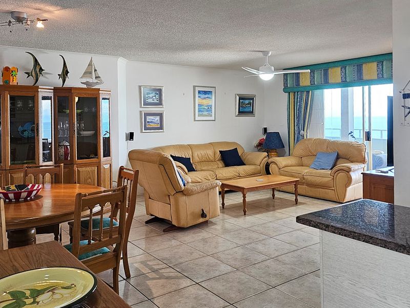 Spacious open-plan living and dining area featuring tiled flooring, a ceiling fan, and direct access to a balcony with ocean views.